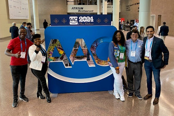 Five people pose for photo in front of large AAO logo. 