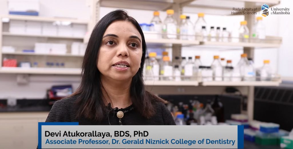 Dr. Devi Atukorallaya in her lab. Text reads Devi Atukorallaya, BDS, PhD, Associate Professor, Dr. Gerald Niznick College of Dentistry. 