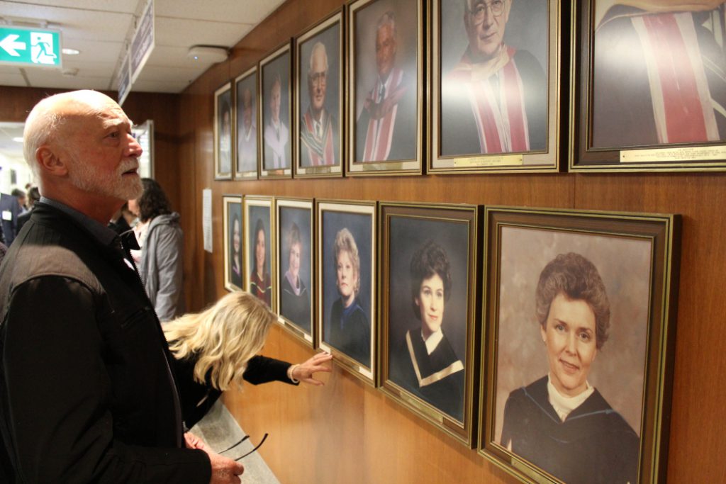 Two alumni look at photos of dean's of the Dr. Gerald Niznick College of Dentistry and the directors of the School of Dental Hygiene on a wall. 