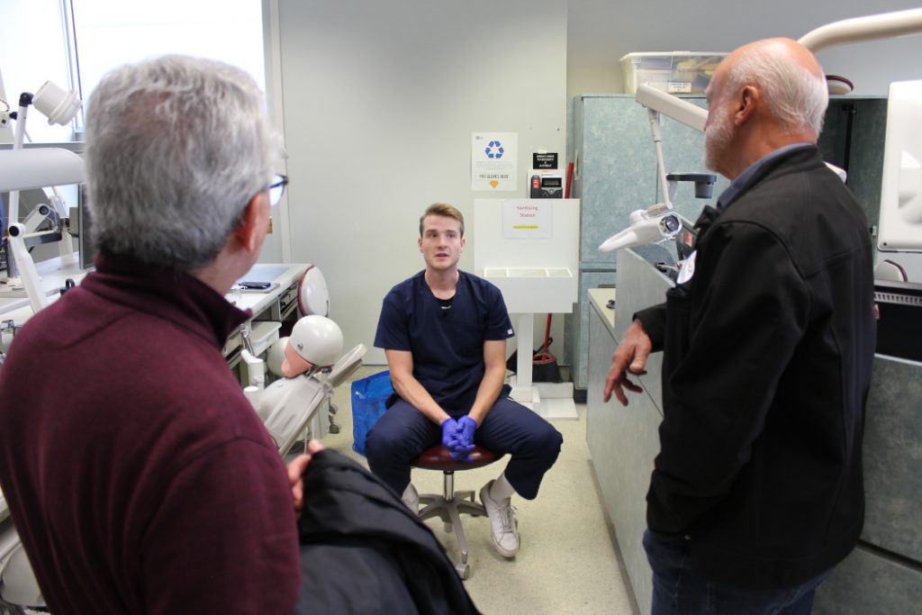 Two alumni talk with a student in a lab. 