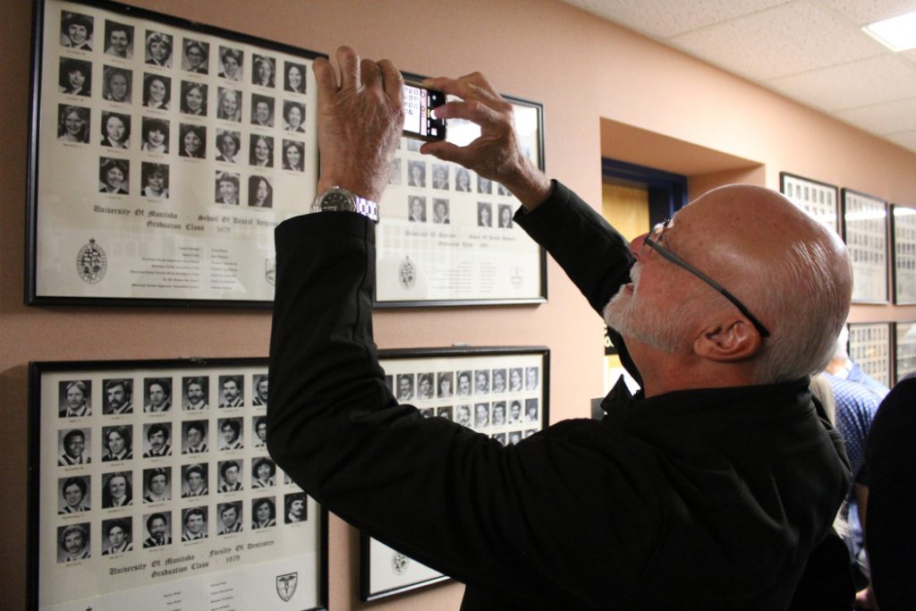 An alumnus takes a photo of graduation class photos on a wall with a mobile phone. 