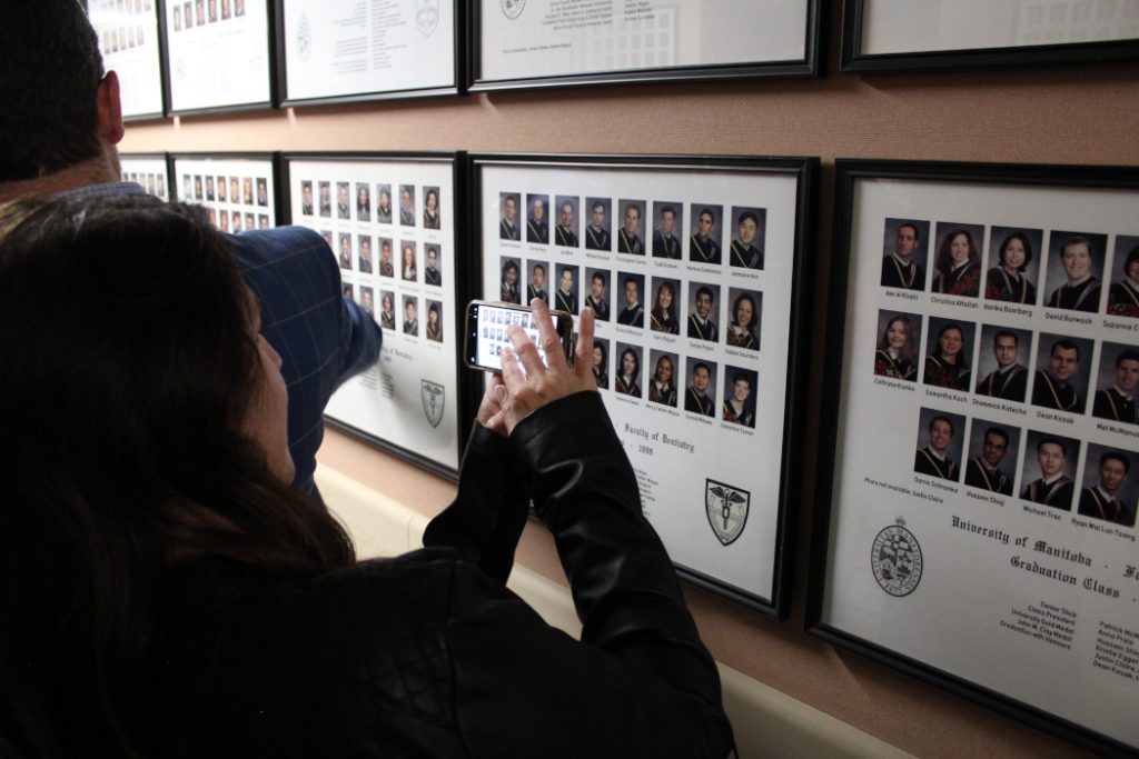 An alumnus takes a photo of graduation class photos on a wall with a mobile phone. 