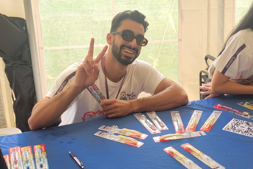 A student gives a peace sign while holding a packaged toothbrush. 