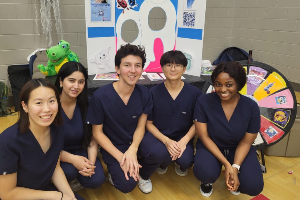 Five students pose for a photo. Their display is set up behind them. 