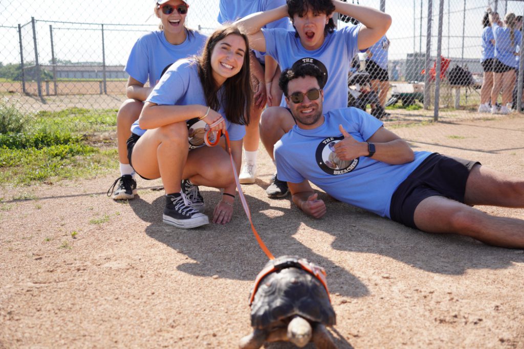 Five people pose for a photo with a turtle on a leash. 