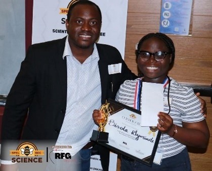 Two people pose for a photo. One person is holding a certificate and trophy. 