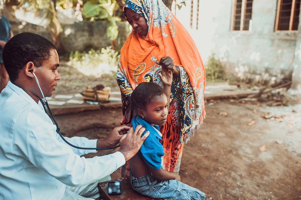 A doctor uses a stethescope to examine a child  in Africa, as the child's mother stands nearby.