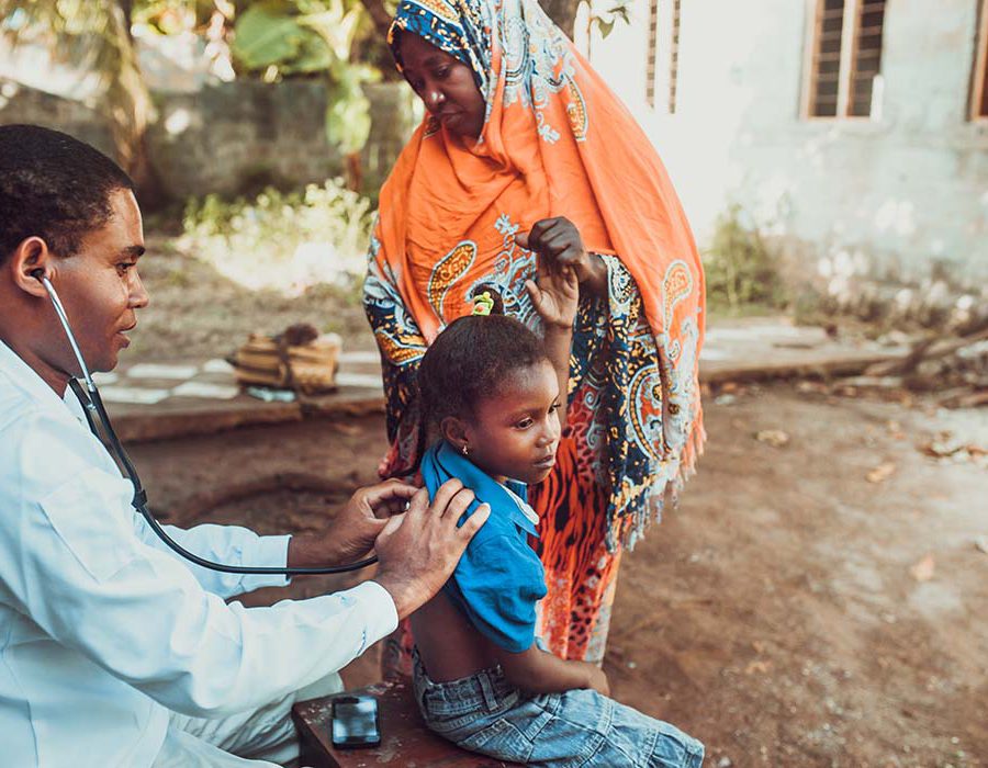 A doctor uses a stethescope to examine a child in Africa, as the child's mother stands nearby.