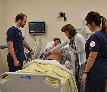 Nursing students attend to a manikin in a bed at the at the College of Nursing's skills lab.