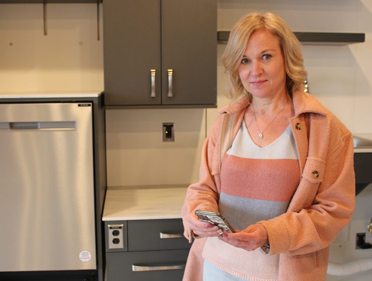 Jacquie Ripat standing with a smartphone inside an apartment suite.