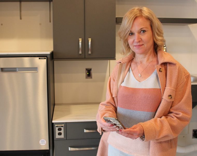 Jacquie Ripat standing with a smartphone inside an apartment suite.