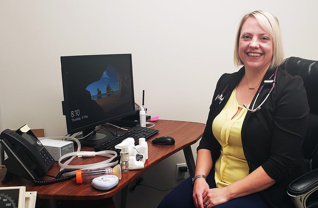 Karen McElroy sits next to a computer with respiratory devices on the desk.