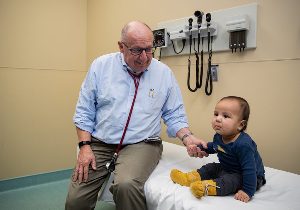 Brian Postl holds a small child's hand in an examination room.