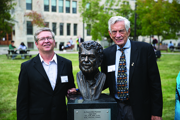 Keith Fowke and Allan Ronald pose with a bust of Dr. Frank Plummer.