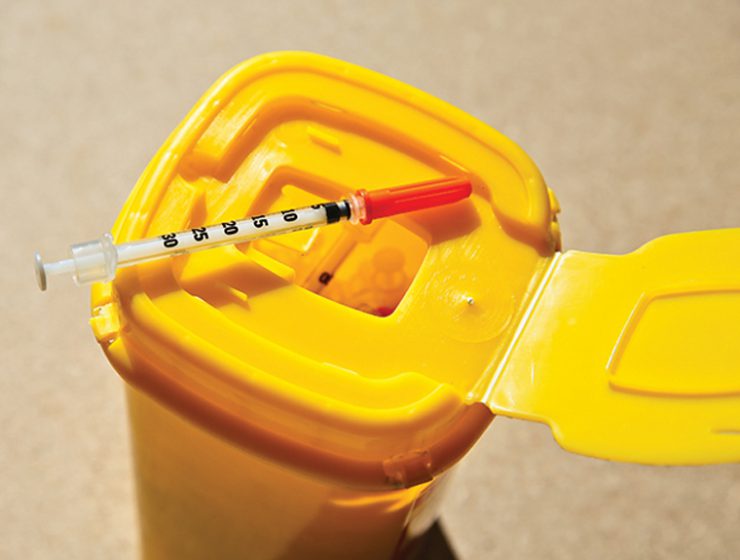 A syringe on top of a plastic disposal box.