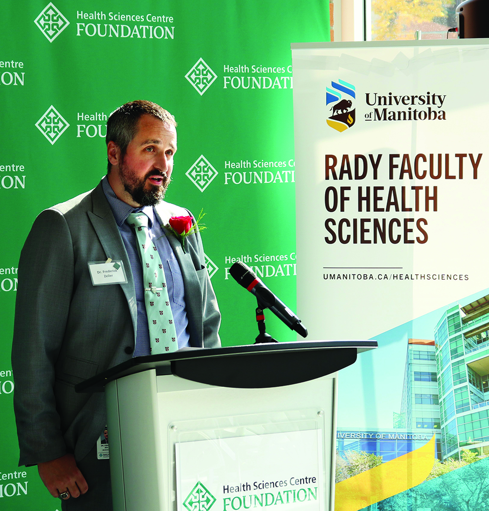 Frederick Zeiler speaks at an announcement in front of signs for the Health Sciences Centre Foundation and Rady Faculty of Health Sciences.