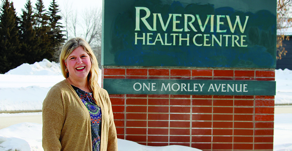 Genevieve Thompson stands by a sign outside Riverview Health Centre.