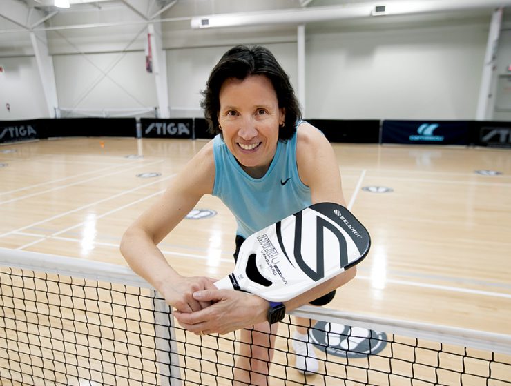 Sandra Webber holds a pickleball racquet and leans over a net.
