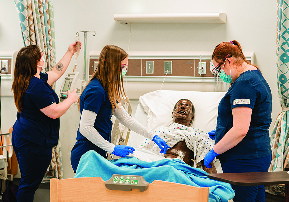 Three female nursing students working with a manikin in a hospital-style bed.