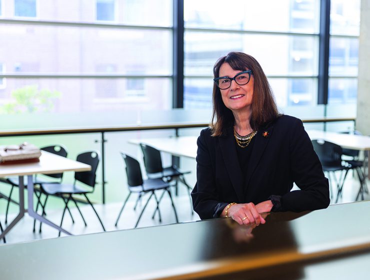 Dr.-Silvia-Alessi-Severini stands in a brightly lit room with several chairs and tables behind her, next to a large window.