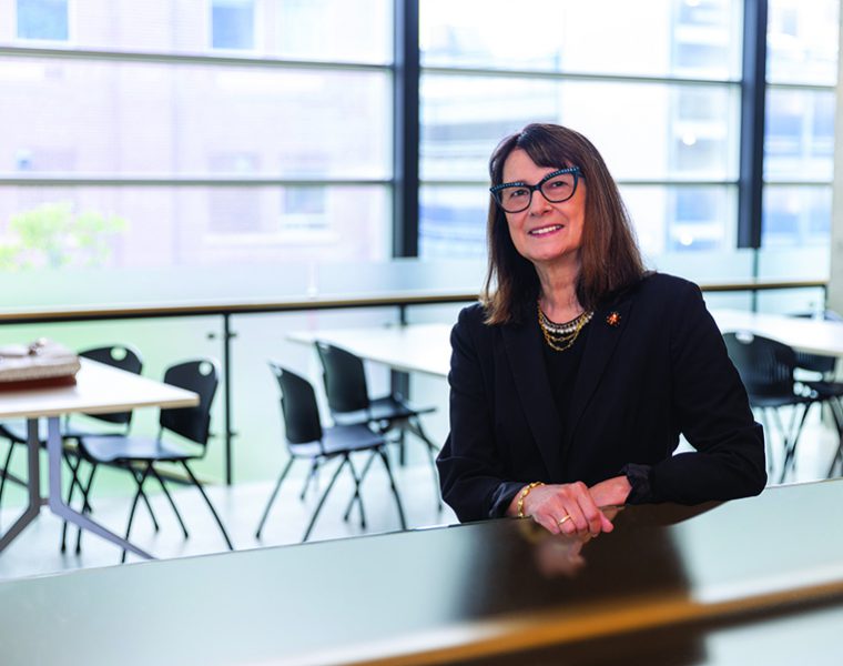 Dr.-Silvia-Alessi-Severini stands in a brightly lit room with several chairs and tables behind her, next to a large window.