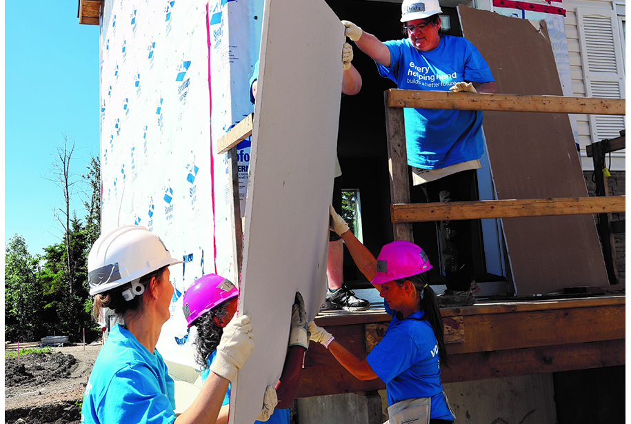 Workers passing a piece of drywall to another worker.