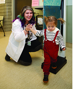 A physician kneeling next to a little girl wearing pigtails.