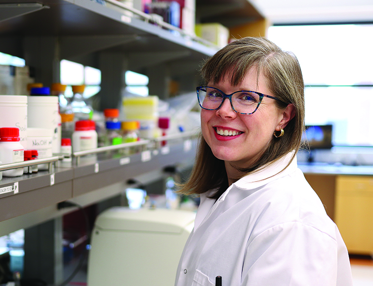 Jillian Stobart stands in a lab , wearing a white coat.