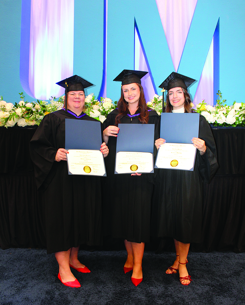 Laura Warkentin, Brooke-Lyn Wahoski and Emily Howarth hold their parchments at convocation. Each is wearing a convocation cap, gown and red shoes.