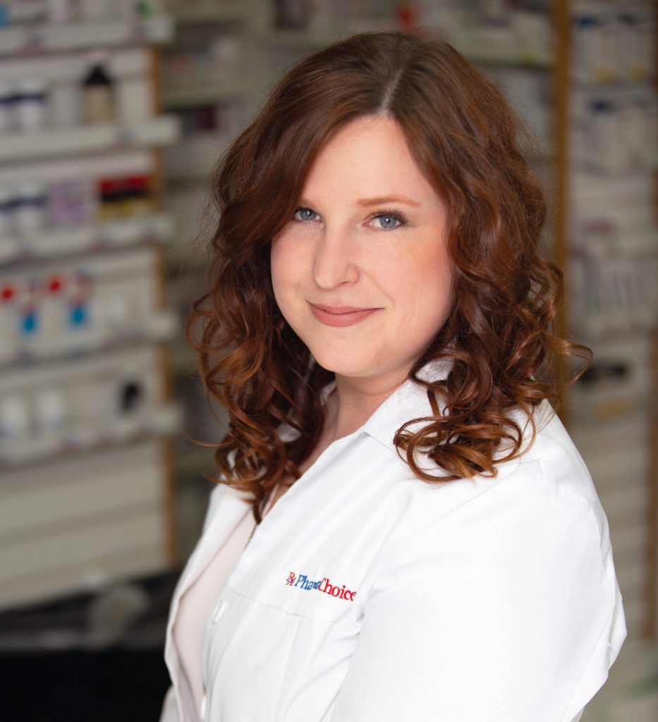 Portrait of Alia Marcinkow in a pharmacy. She is wearing a pharmacist's white coat. 