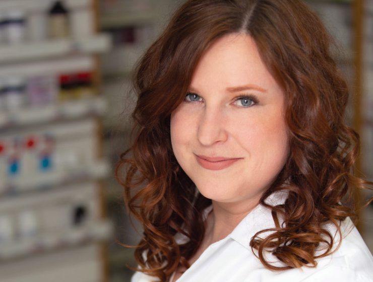 Portrait of Alia Marcinkow in a pharmacy. She is wearing a pharmacist's white coat.