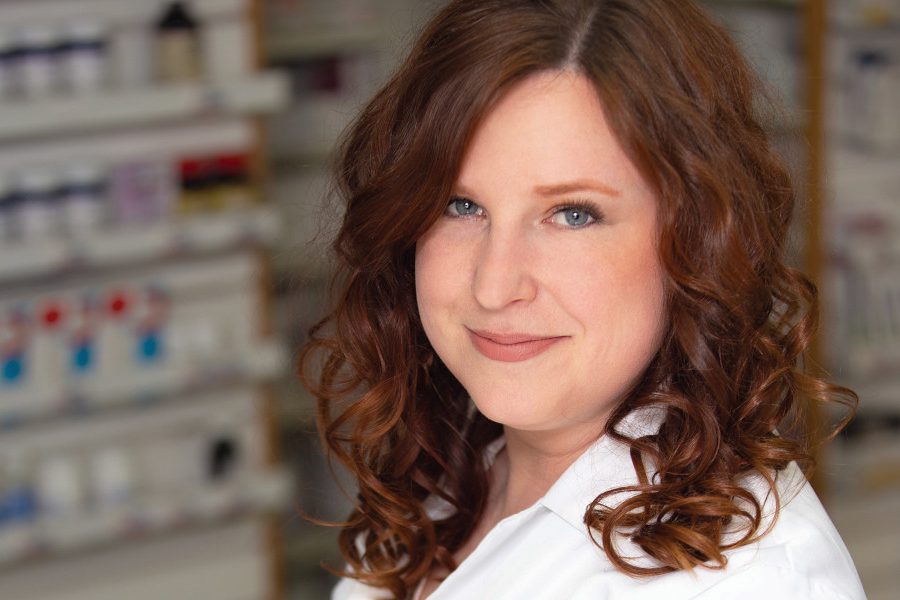 Portrait of Alia Marcinkow in a pharmacy. She is wearing a pharmacist's white coat.