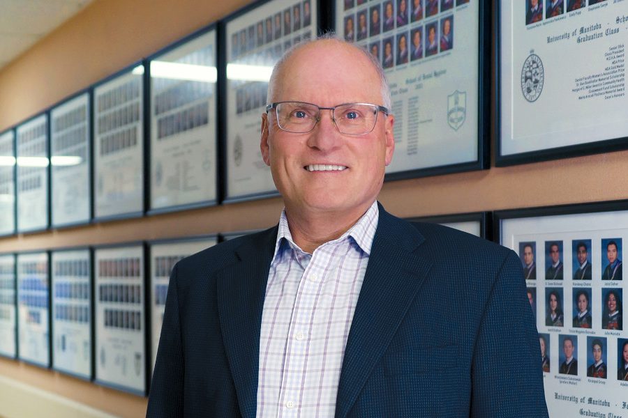 Portrait of Dr. John Perry. Dentistry student graduation photos are in frames on the wall behind him.