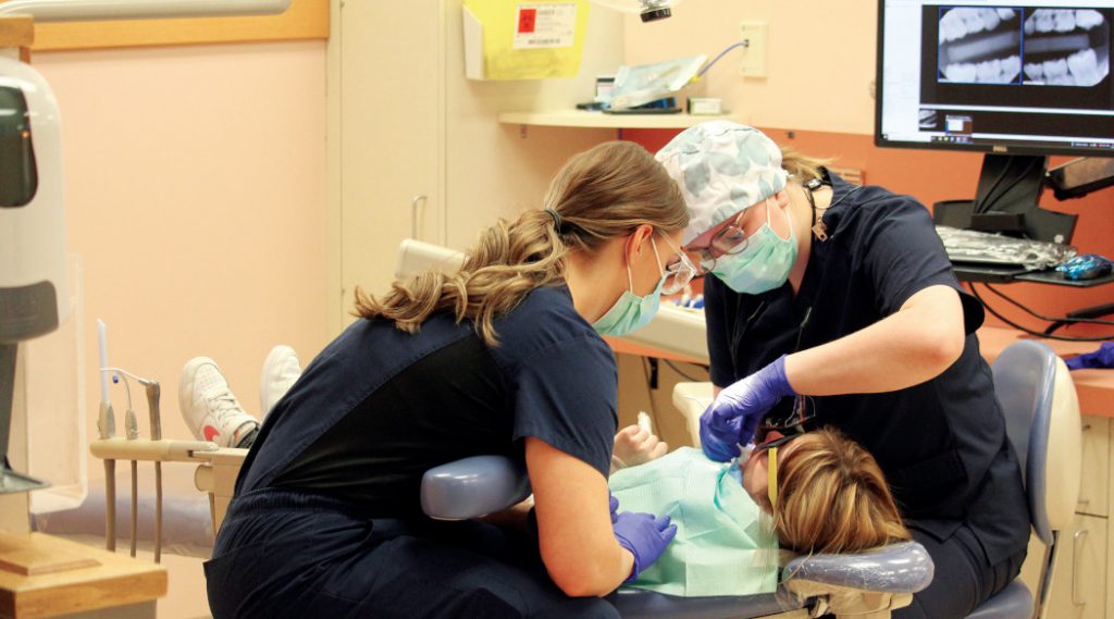 Two students perform a dental procedure on a child laying in a dental chair. 