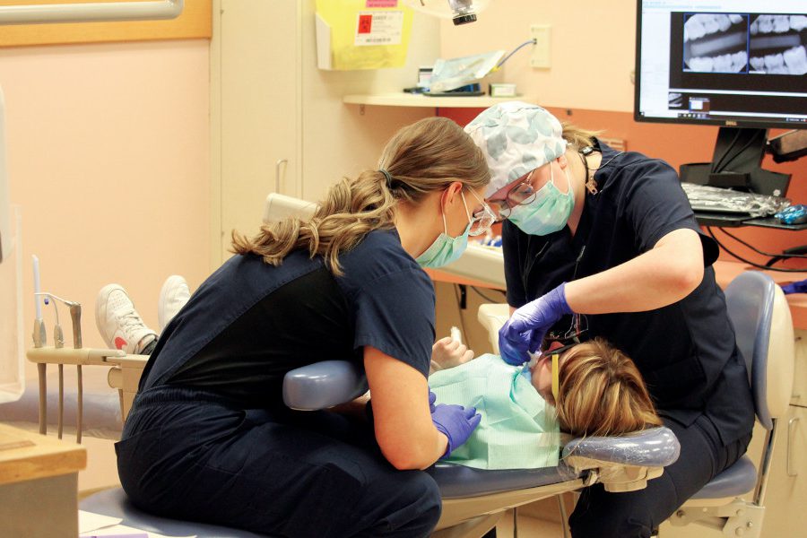 Two students perform a dental procedure on a child laying in a dental chair.