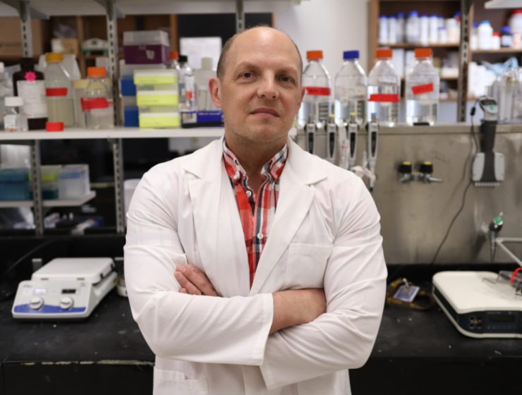 Dr. Jason Kindrachuk stands in his lab. Research equipment is behind him.