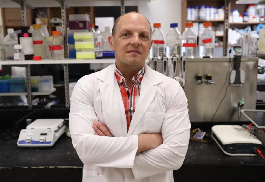 Dr. Jason Kindrachuk stands in his lab. Research equipment is behind him.