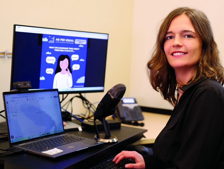 Anna Chudyk sits in front of two computers and a microphone, preparing for a podcast.