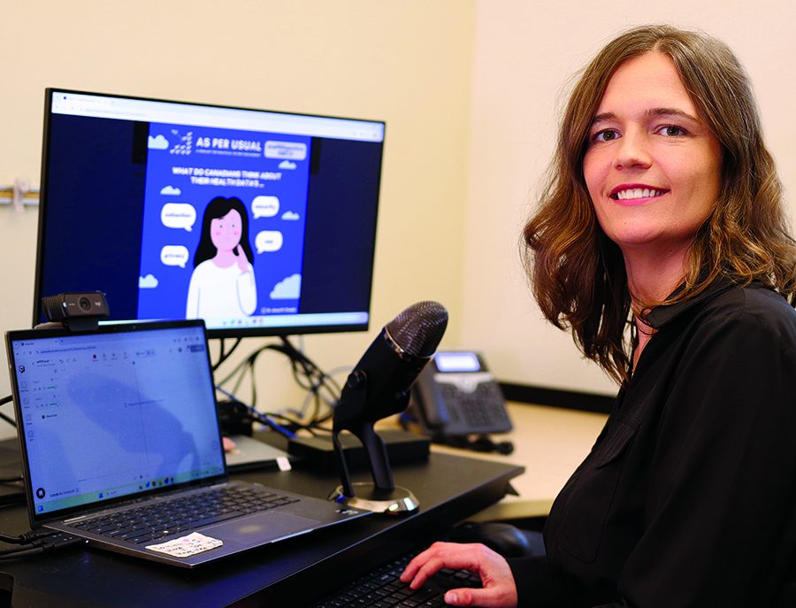 Anna Chudyk sits in front of two computers and a microphone, preparing for a podcast.