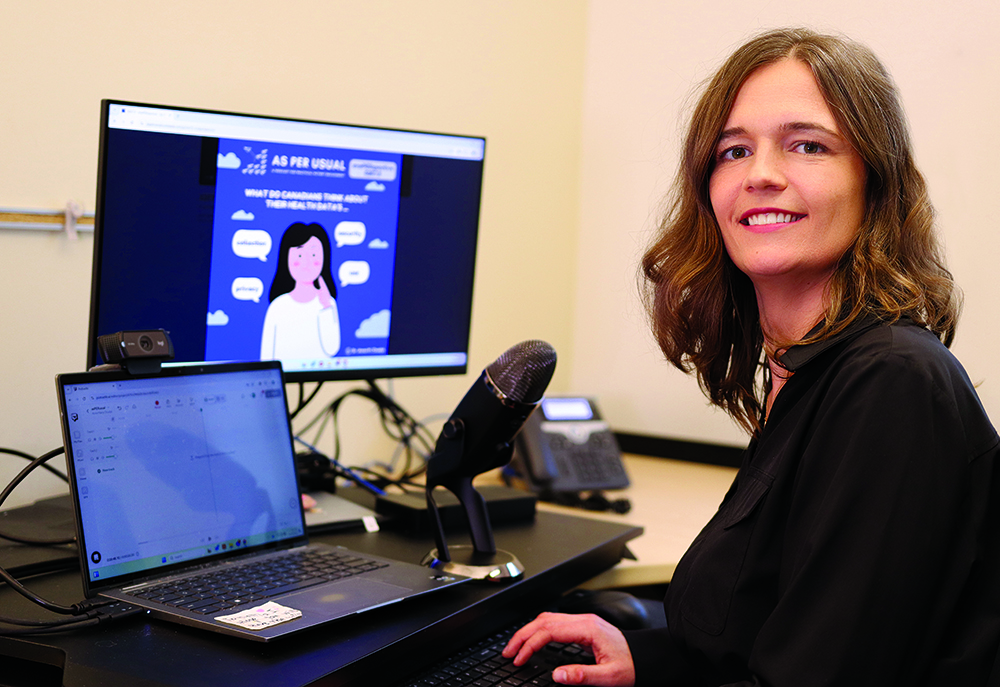 Anna Chudyk sits in front of two computers and a microphone, preparing for a podcast.