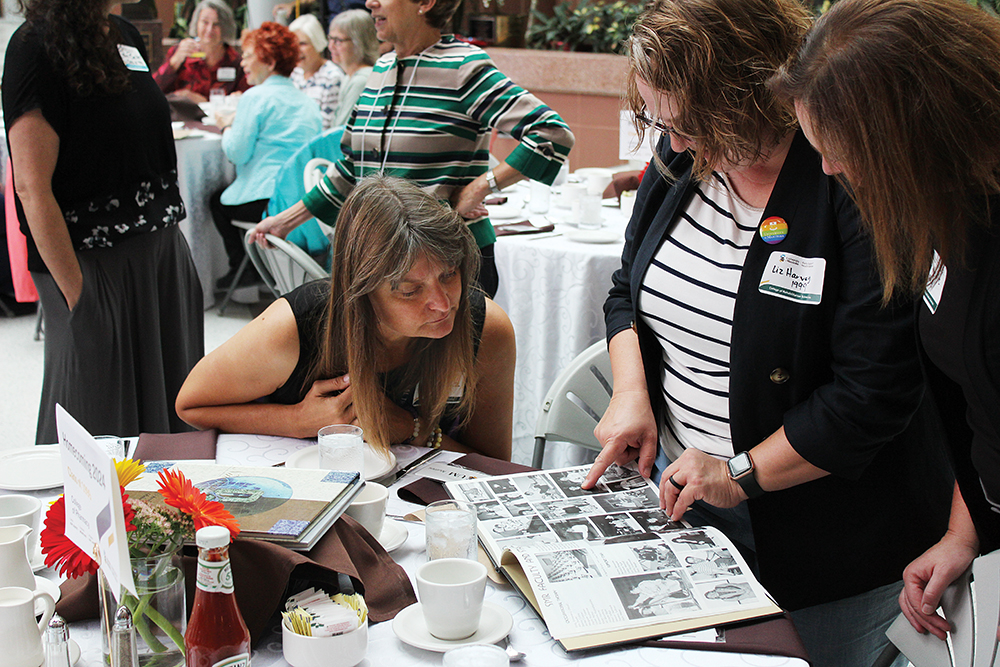 Three alumni are looking at a yearbook. 