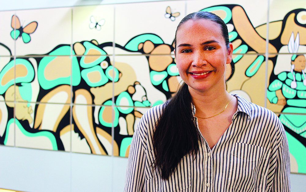 A student stands in front of an Indigenous mural at the College of Nursing.