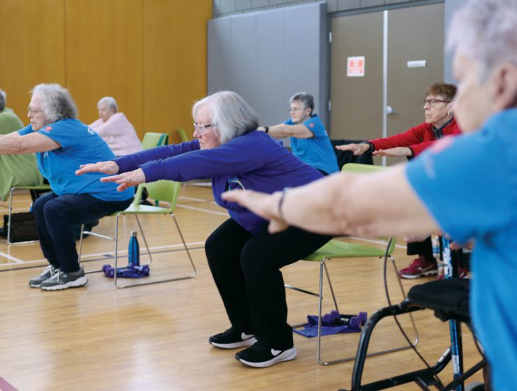 Seven older adults do chair squats with their arms out in front of them.