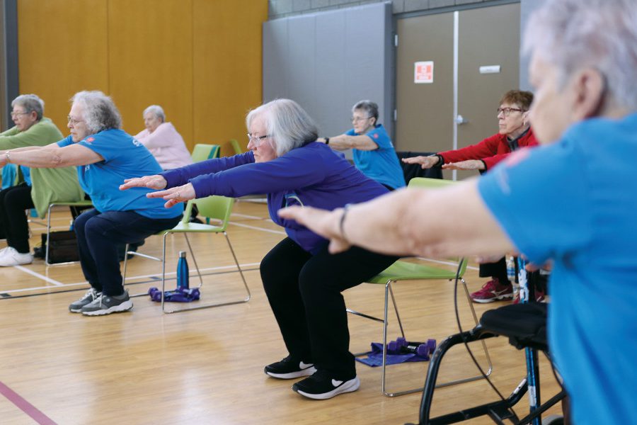 Seven older adults do chair squats with their arms out in front of them.