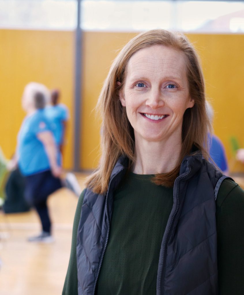 Portrait of Dr. Kathryn Sibley. Older adults do exercises behind her. 