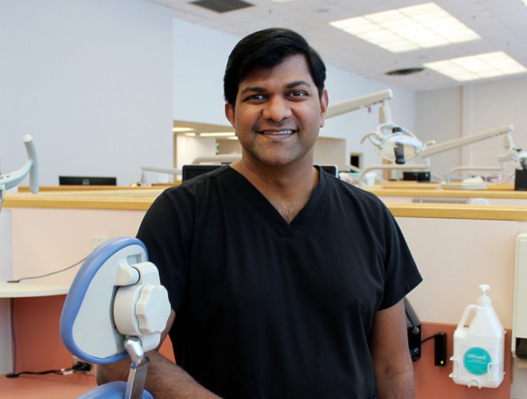 Portrait of Dr. Anil Menon in a dental clinic. He is leaning against a dental chair.