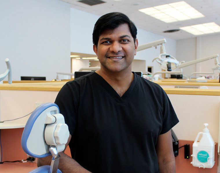 Portrait of Dr. Anil Menon in a dental clinic. He is leaning against a dental chair.