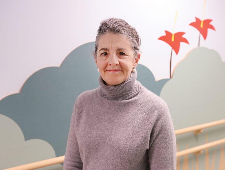 Ana Hanlon-Dearman stands in front of a colourfully painted wall.