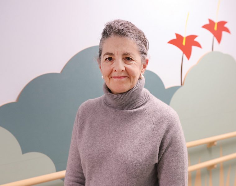 Ana Hanlon-Dearman stands in front of a colourfully painted wall.