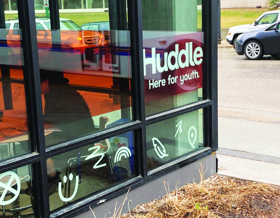 A building with text on a window that reads "Huddle, here for youth."